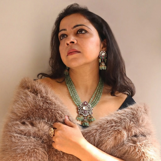 Woman wearing a fur coat and jewelry against a plain background